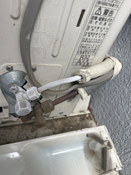 熊谷市で対応したエアコン修理の施工後写真。室外機の冷媒配管接続部とサービスバルブ付近が写り、外されたカバーと、ラベルのR32表示が見える。
