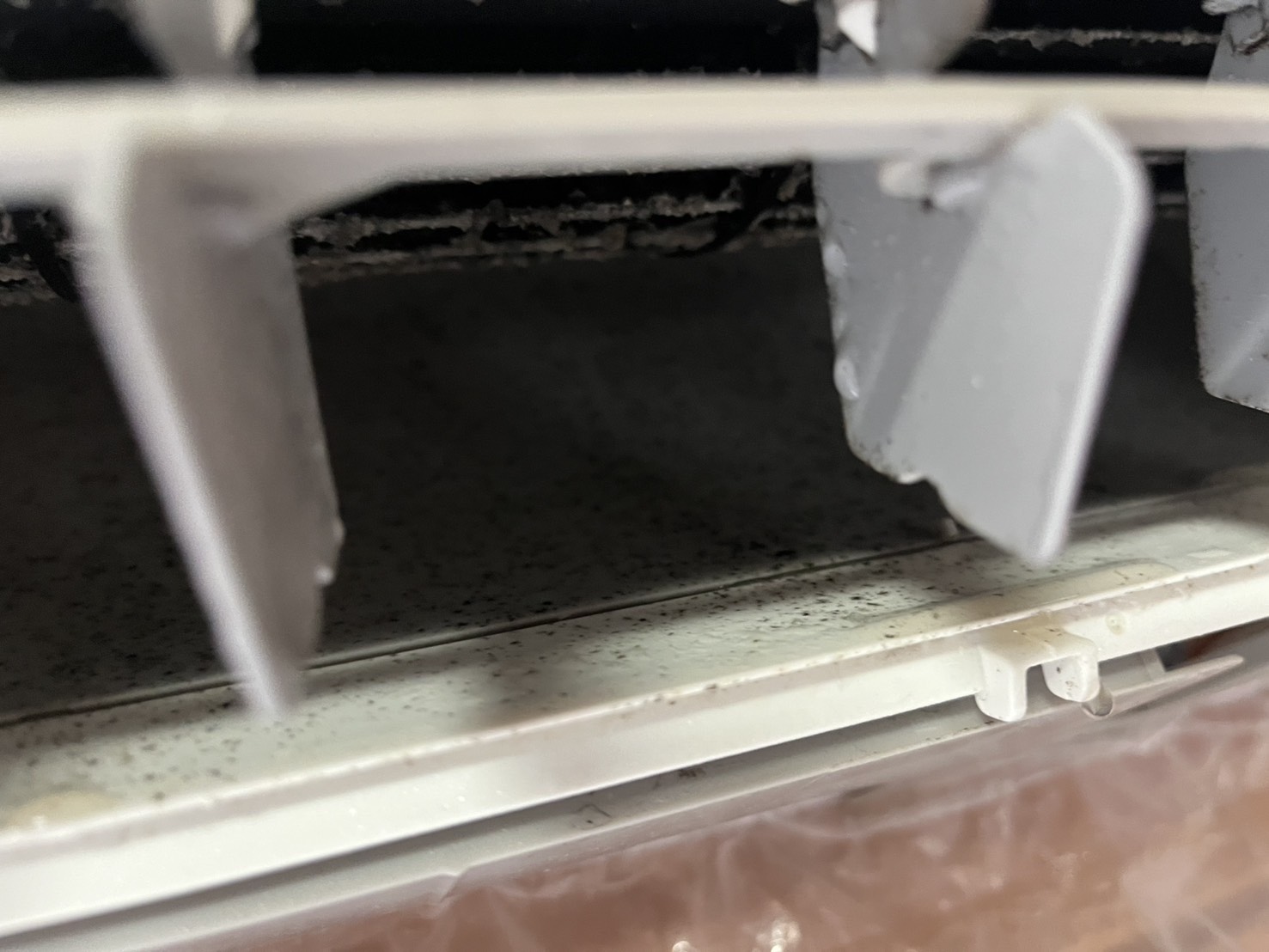 エアコン室内機の送風口内部。白い風向板や周辺部品に黒色の点状・筋状の付着物が見られる施工前の状態